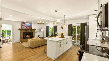 Una cocina moderna con una isla central, un área de comedor con sofá y una sala de estar con chimenea.