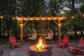 Una chimenea con dos sillas colgantes y una pérgola con luces de cuerda.