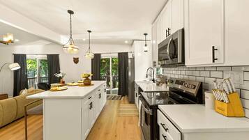 Una cocina moderna con armarios blancos, una isla central, electrodomésticos de acero inoxidable e iluminación colgante.