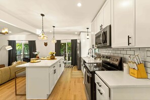 A modern kitchen with white cabinetry, a central island, stainless steel appliances, and pendant lighting.