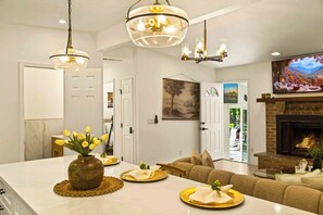 A modern living room with a fireplace, a dining area with a vase of flowers, and a painting on the wall.