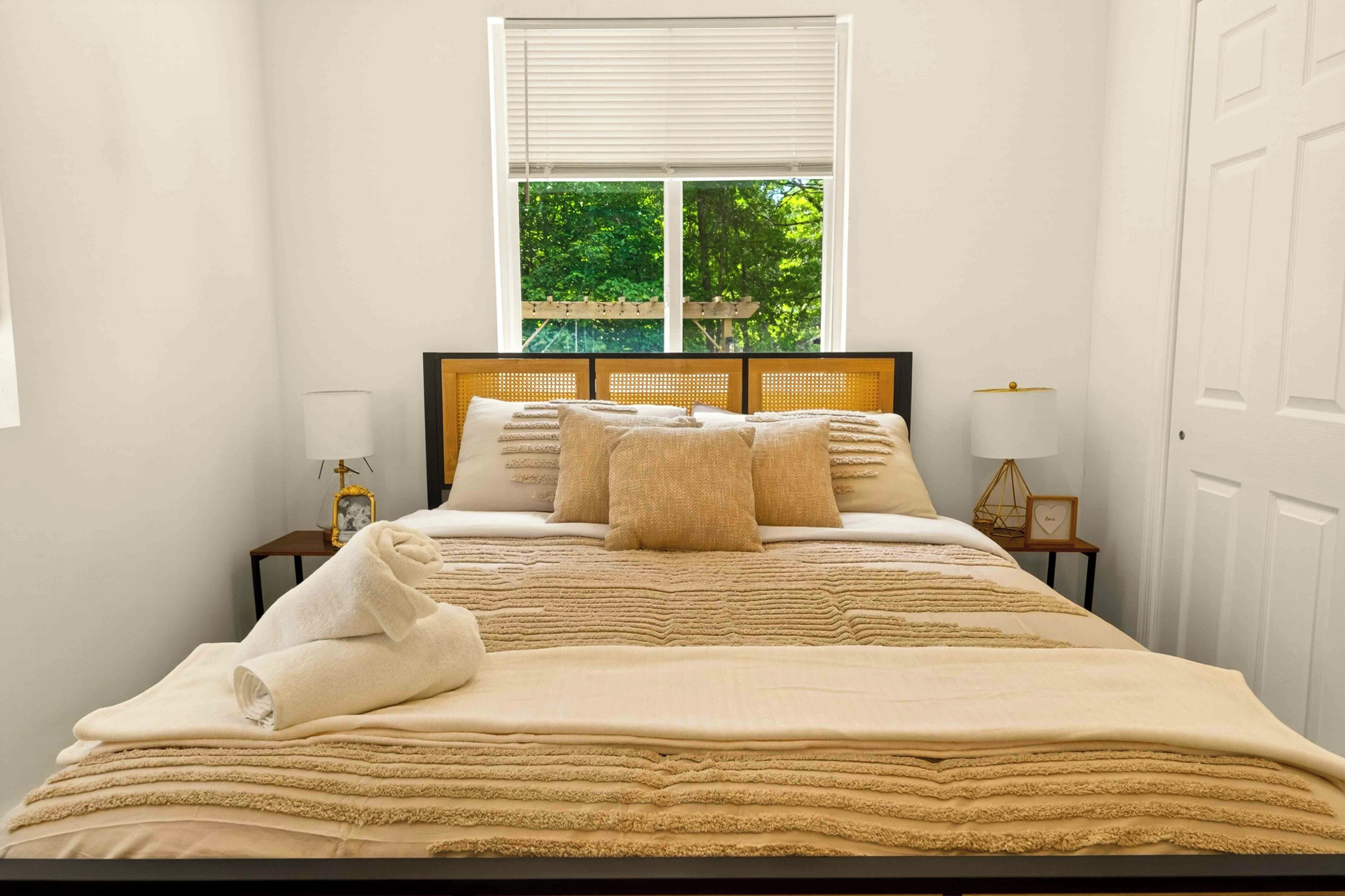 A neatly made bed with a headboard, a window with blinds, and two bedside tables with lamps.