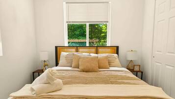A neatly made bed with a headboard, a window with blinds, and two bedside tables with lamps.