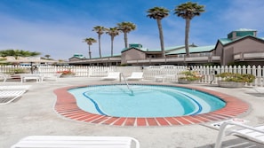 A swimming pool with a brick border, surrounded by lounge chairs and a white fence.