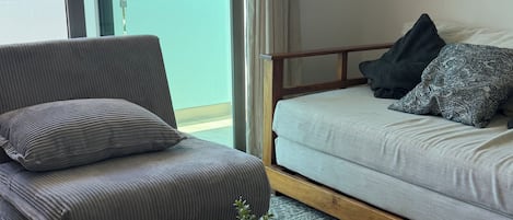 Ein modernes Wohnzimmer mit einer Couch, einem Couchtisch mit Gebäck und Blick auf Palmen durch große Fenster.