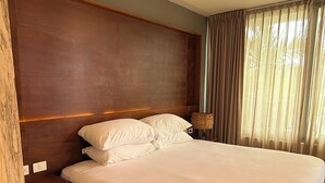 Ein Hotelzimmer mit einem großen Bett, einem Holz-Kopfteil, einem Nachttisch, einer Lampe und einem fenster mit Vorhängen.
