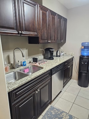 A kitchen with dark wooden cabinets, a granite countertop, a stainless steel sink, a coffee maker, and a water dispenser. - Stay in the Heart of Downtown Atlanta Sleeps 4 Perfect for Getaways. (Atlanta)