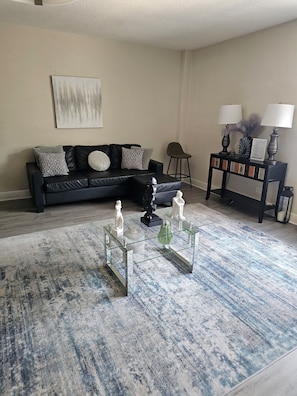 A living room with a black sectional sofa, a glass coffee table with decorative items, and a console table with lamps and a vase. - Stay in the Heart of Downtown Atlanta Sleeps 4 Perfect for Getaways. (Atlanta)