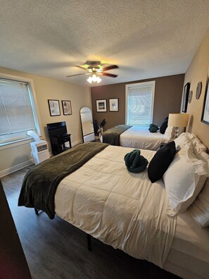 A hotel room with two beds, a ceiling fan, a desk, and a window with blinds. - Stay in the Heart of Downtown Atlanta Sleeps 4 Perfect for Getaways. (Atlanta)