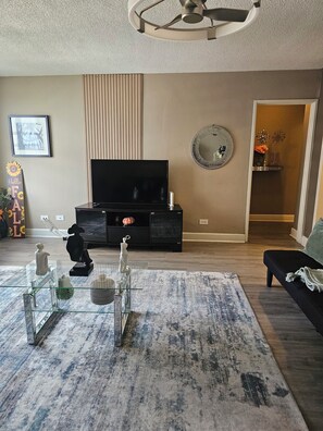 A living room with a flat-screen TV, a glass coffee table with decorative items, a patterned rug, and a dark-colored sofa. - Stay in the Heart of Downtown Atlanta Sleeps 4 Perfect for Getaways. (Atlanta)
