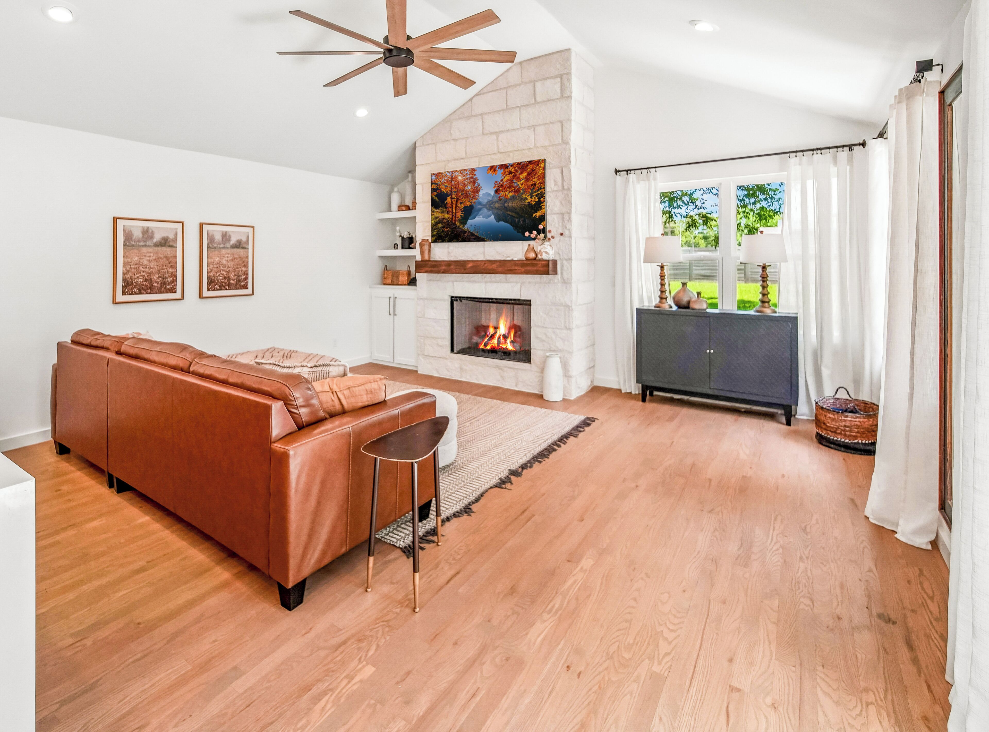 A modern living room with a fireplace, a sectional sofa, and a view of the outdoors through a large window.