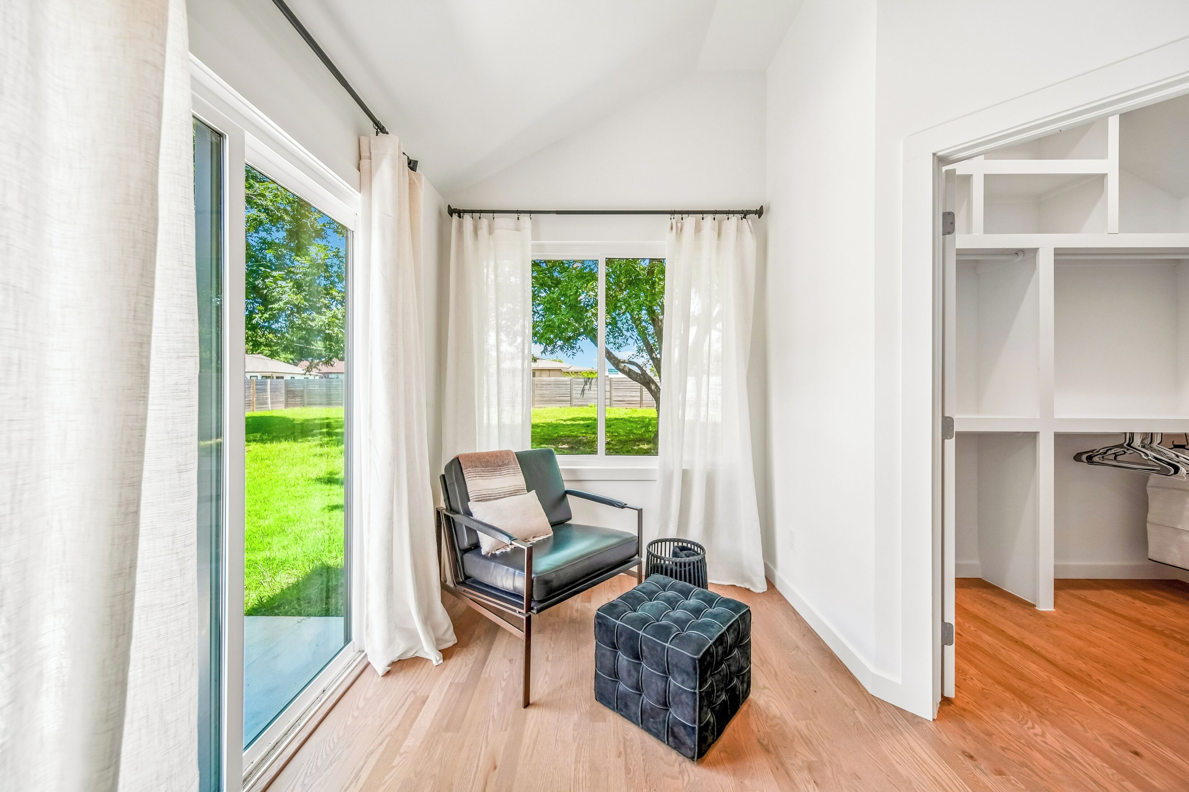 A room with a large window, a chair, a small ottoman, and a white closet.