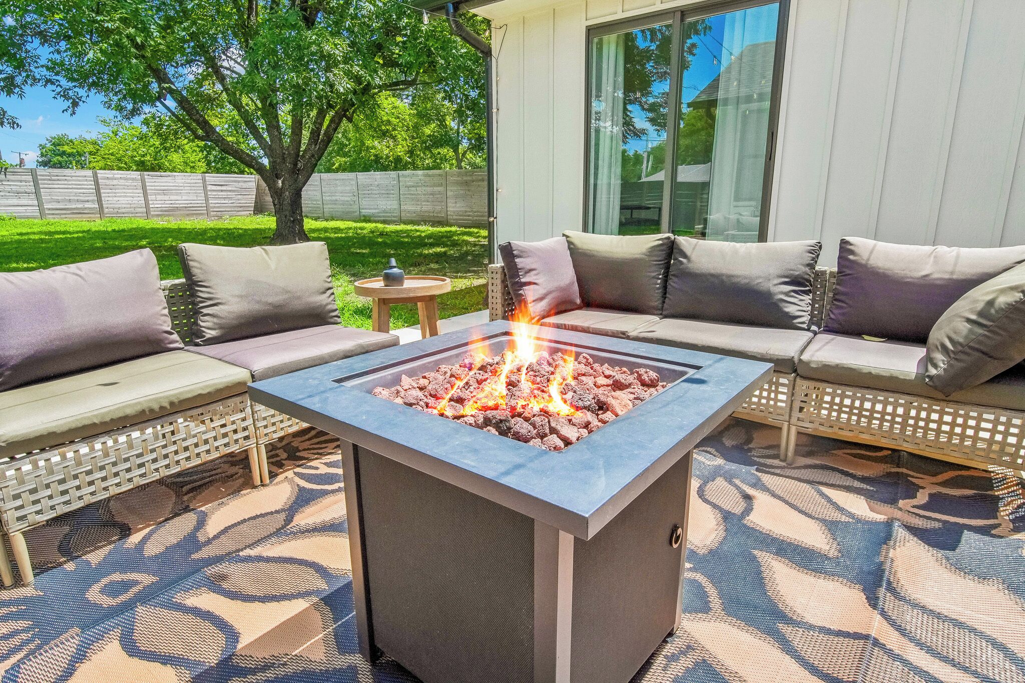 A fire pit with a square stone design, surrounded by outdoor seating with cushions.