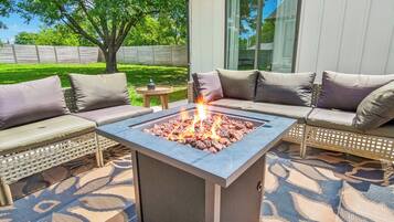 A fire pit with a square stone design, surrounded by outdoor seating with cushions.