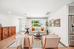 Una sala de estar moderna con un sofá, una mesa de centro y sillas, un mueble de madera y un ventanal con vistas a la vegetación.