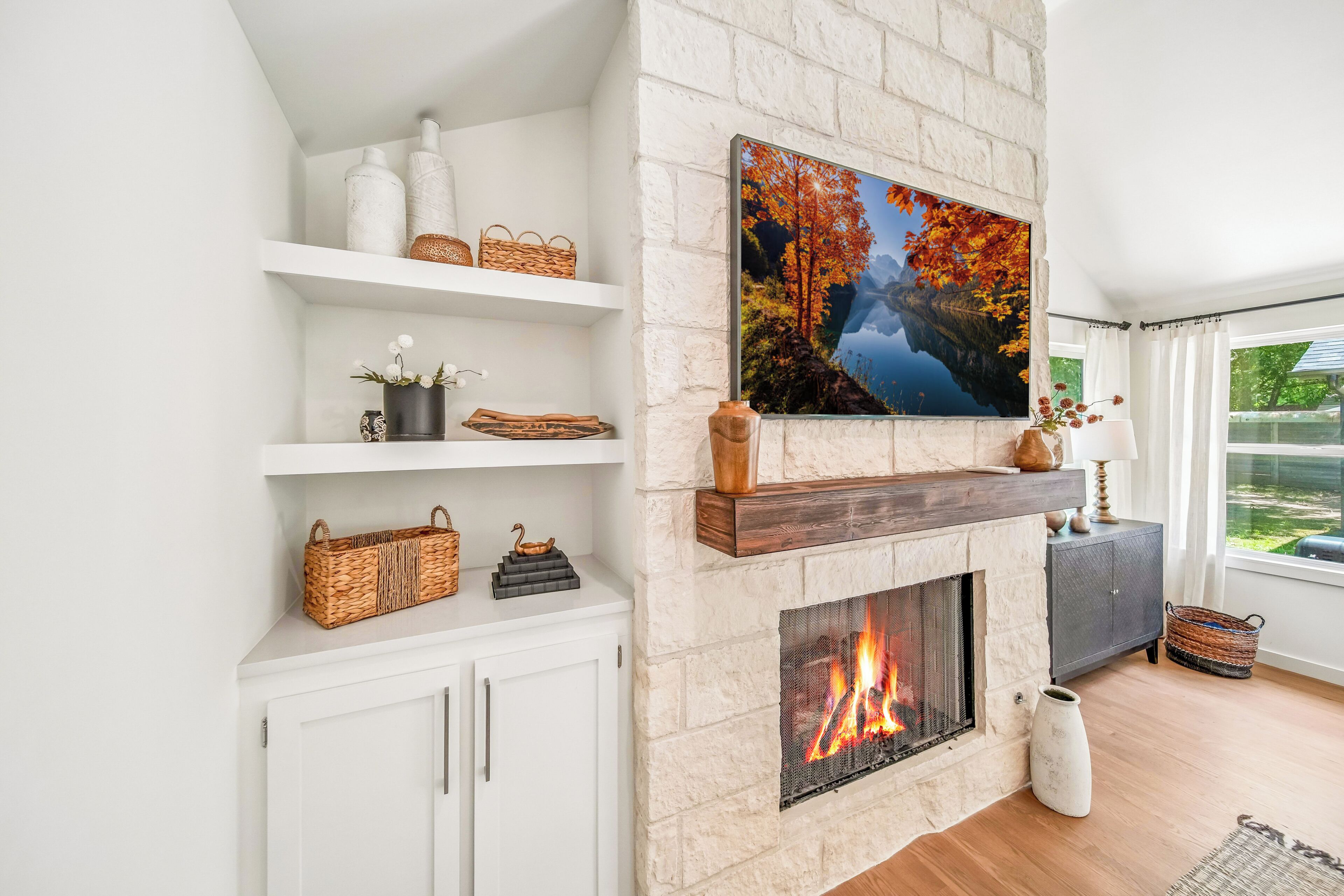 A modern living room with a fireplace, white shelves, and a large window.