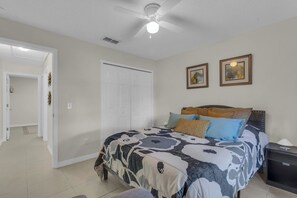 Une chambre à coucher avec un lit, une table de chevet, un ventilateur de plafond et une porte.