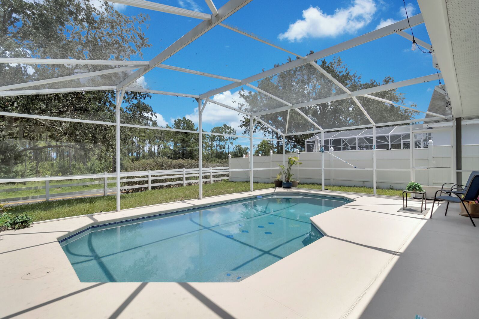 A covered outdoor swimming pool with a white fence, a chair, and potted plants.