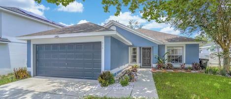 A residential house with a garage, a front porch, and a well-maintained lawn.
