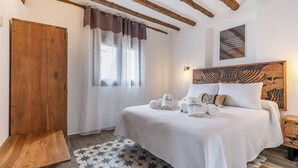 A bedroom with a bed, a wooden wardrobe, a window with curtains, and a wall with a framed artwork. - Casa Rural Museo del Trovo y Aguardiente Murtas by Ruralidays (Granada)
