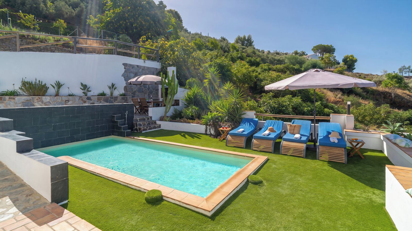 Une piscine bordée de pierres, entourée de gazon synthétique et dotée de chaises longues.