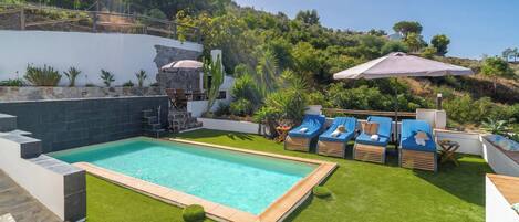 A swimming pool with a stone border, surrounded by artificial grass, and equipped with lounge chairs.