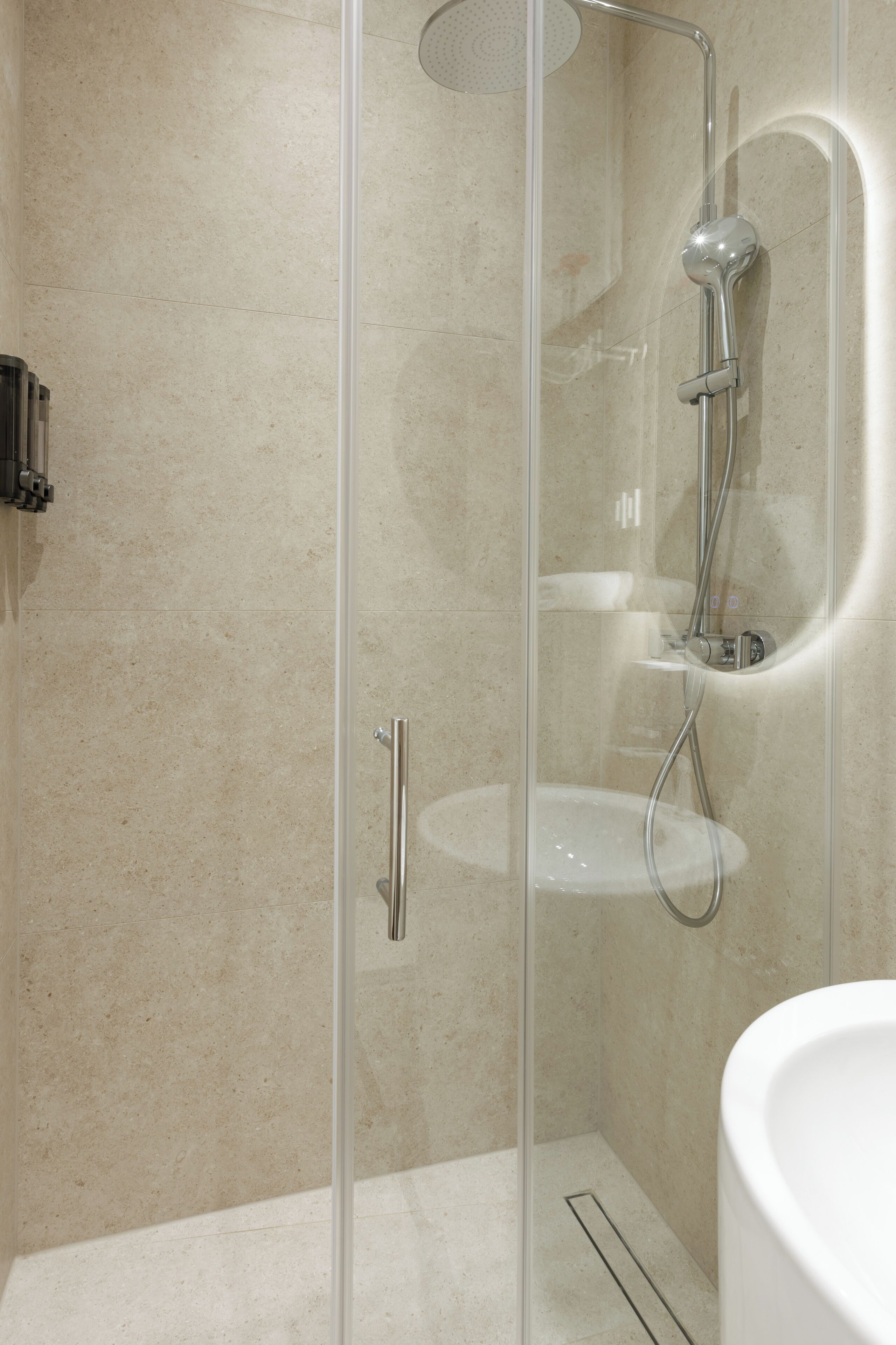 A modern bathroom with a glass-enclosed shower, a white sink, and a handheld showerhead.