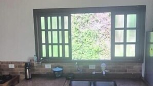 A kitchen with a window, a sink, and a dining area with a table and chairs. - Country house on the reservoir with beach, kayaking, fishing and waterfall. (Juquitiba)