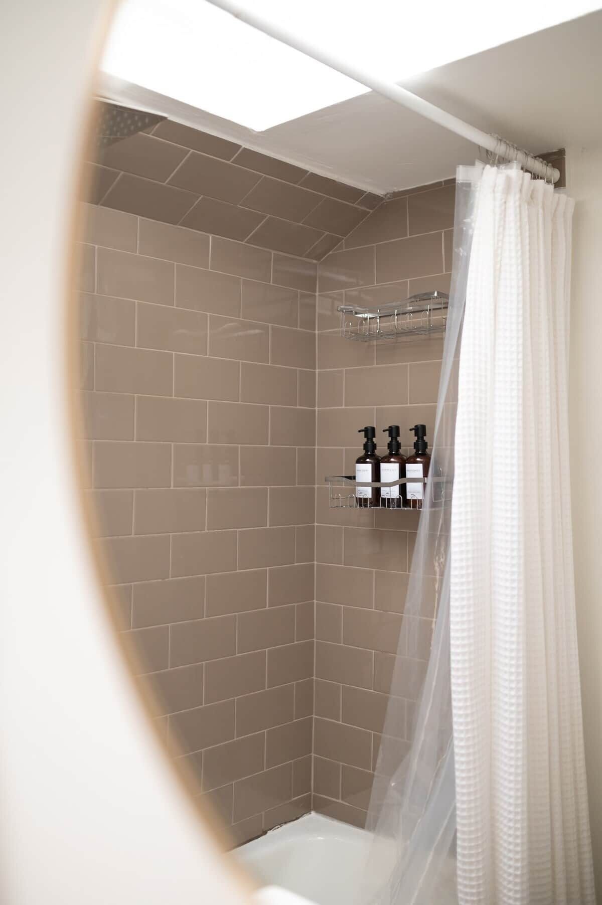 A shower area with beige tiles, a glass shower caddy, and a white shower curtain.