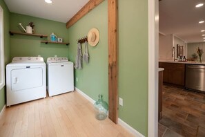 A laundry area with two white washing machines, a glass bottle, and wooden shelves with items. - 8-Acre Retreat with Trails, 7 Min to Killington (Plymouth)