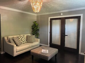 A living room with a sofa, patterned cushions, a coffee table, a plant, and a door with blinds. - Modern 4BR Retreat Near Little Saigon Fast Wi-Fi & Free Parking (Houston)