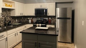 Una cucina moderna con mobili bianchi, un frigorifero in acciaio inossidabile e un piano di lavoro nero.