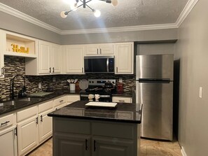 A modern kitchen with white cabinets, a stainless steel refrigerator, and a black countertop. - Modern 4BR Retreat Near Little Saigon Fast Wi-Fi & Free Parking (Houston)