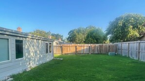 Un giardino recintato da una staccionata in legno, un prato verdeggiante e una casa con un garage.