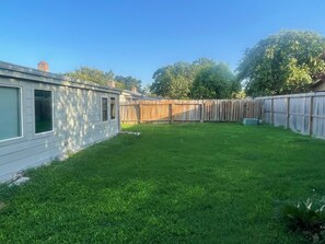 A backyard with a wooden fence, a grassy lawn, and a house with a garage. - Modern 4BR Retreat Near Little Saigon Fast Wi-Fi & Free Parking (Houston)