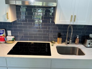 A kitchen with a black induction cooktop, a stainless steel sink, and a window above the counter. - Beach Haven - ramp access, 2 min. to beach, Shibumi shade, lighthouse display. (Hilton Head Island)