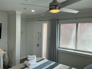 A hotel room with a bed, a ceiling fan, a window with blinds, and a door. - Beach Haven - ramp access, 2 min. to beach, Shibumi shade, lighthouse display. (Hilton Head Island)