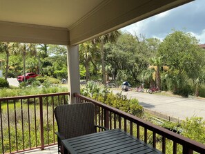 A balcony with a wicker chair and a table, overlooking a parking area with bicycles and a red vehicle. - Beach Haven - ramp access, 2 min. to beach, Shibumi shade, lighthouse display. (Hilton Head Island)