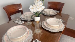 Uma mesa de jantar posta com pratos listrados, copos transparentes e uma orquídea em vaso.