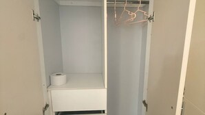 Um closet amplo com uma barra para pendurar roupas, uma prateleira com um rolo de papel higiênico e um conjunto de gavetas.