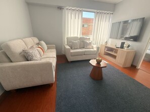 Ein modernes Wohnzimmer mit Sofa, Ohrensessel, Couchtisch und Flachbildfernseher.