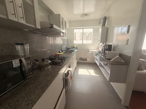A compact kitchen with a gas stove, microwave, and a small sink. - Well-Located Apt Near Airport (San Miguel)