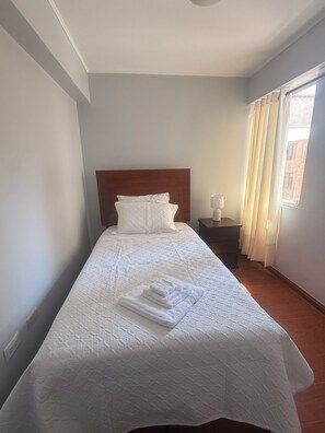 Un lit bien fait, avec une tête de lit, une table de chevet avec une lampe et une fenêtre avec des rideaux.