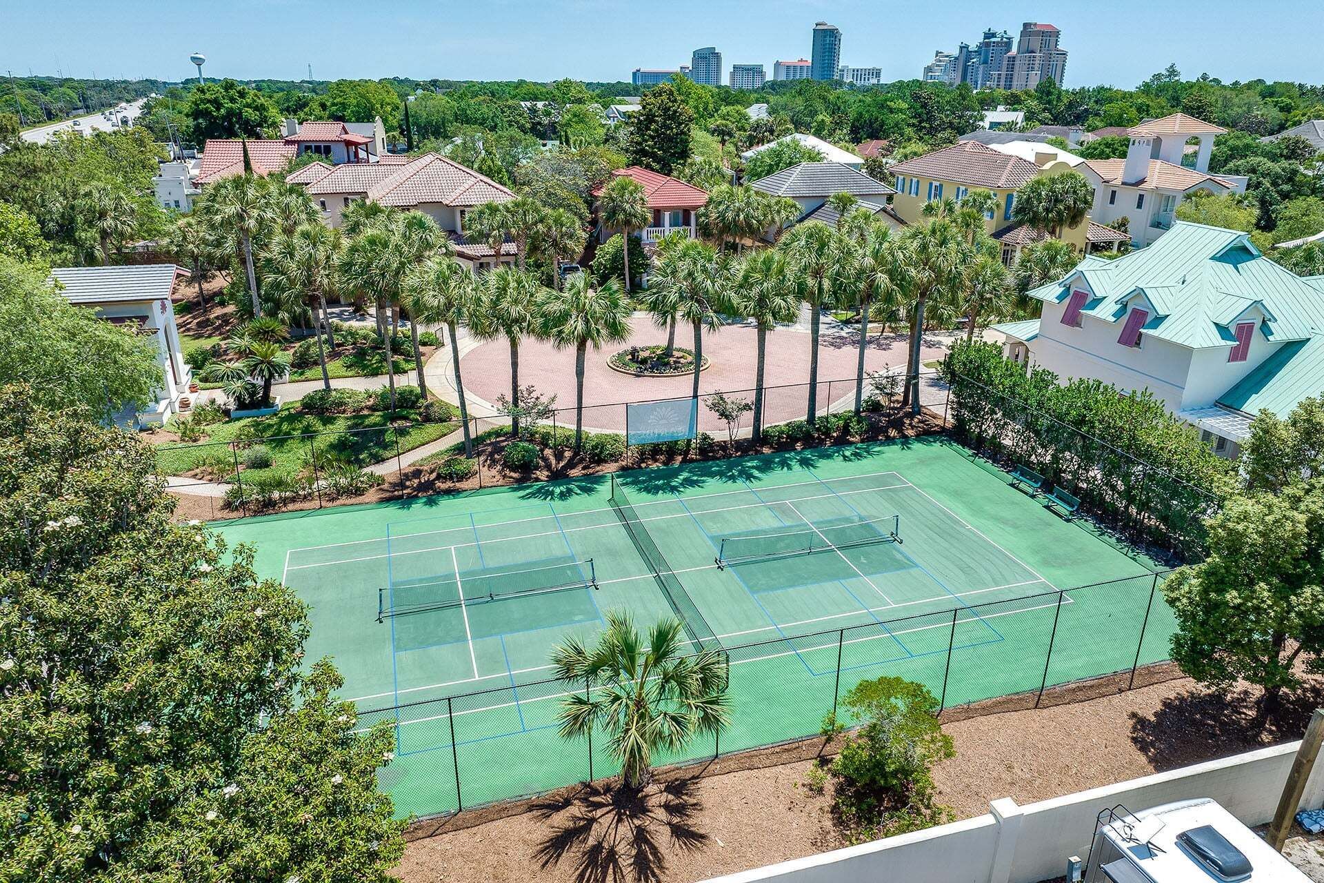 Ein Tennisplatz, umgeben von Wohnhäusern und Palmen.