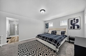A bedroom with a bed, a bedside table, a wall-mounted artwork, and a door leading to a bathroom.