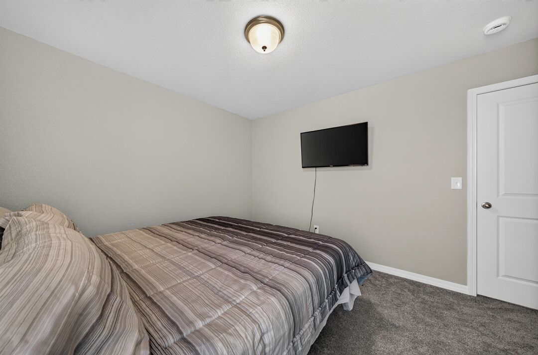 A bedroom with a bed, a television mounted on the wall, and a door.
