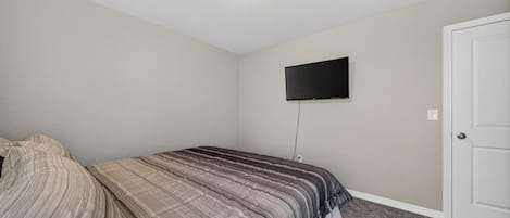 A bedroom with a bed, a television mounted on the wall, and a door.