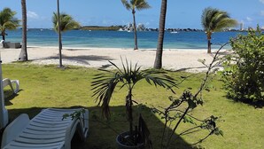 Blick auf einen Strand mit Palmen, einem weißen Liegestuhl und blauem Himmel.
