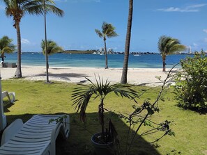 Blick auf einen Strand mit Palmen, einem weißen Liegestuhl und blauem Himmel.
