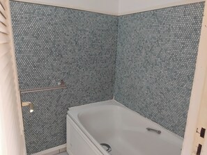 Ein Badezimmer mit einer weißen Badewanne, einer Dusche und einer gefliesten Wand mit Wabermuster.
